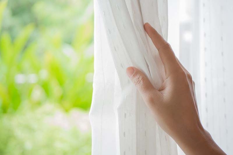 Image of someone pulling back curtain. 5 Tips to Improve Your Indoor Air Quality.