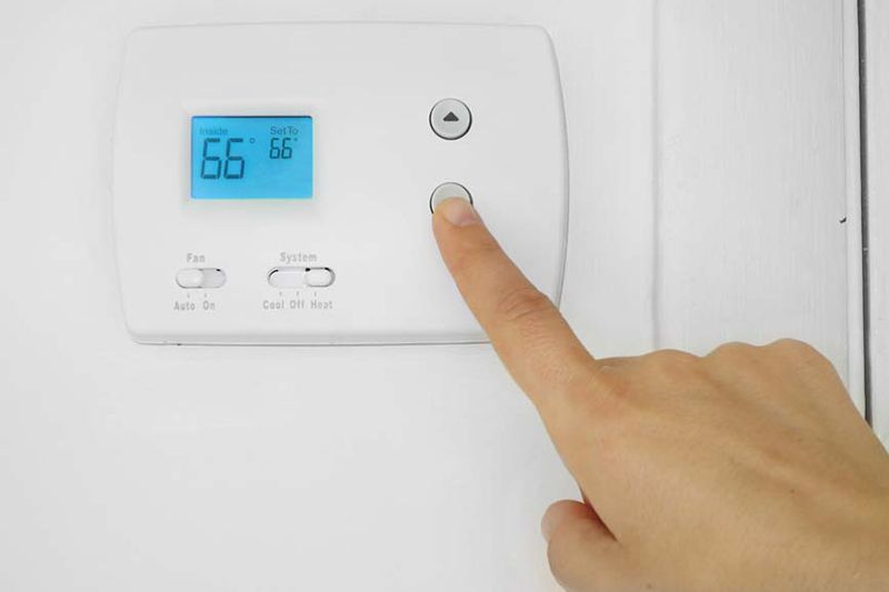 Image of hand on thermostat. What Is the Difference Between a Smart Thermostat and a Regular One?.