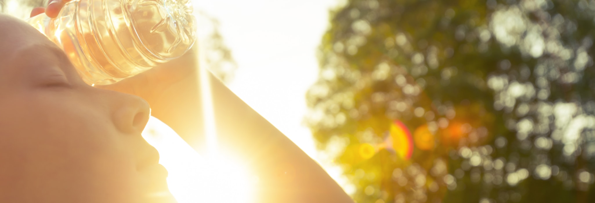 Woman using water bottle to cool down. Fitness and wellbeing concept with female athlete cooling down on a city street. She is holding a water bottle to her head to cool down. The sun is low creating long shadows and some lens flare. Copy space