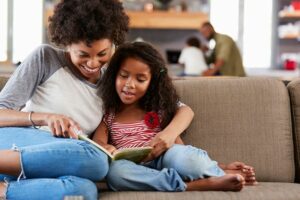 mother and daughter sitting on couch reading a book together.
